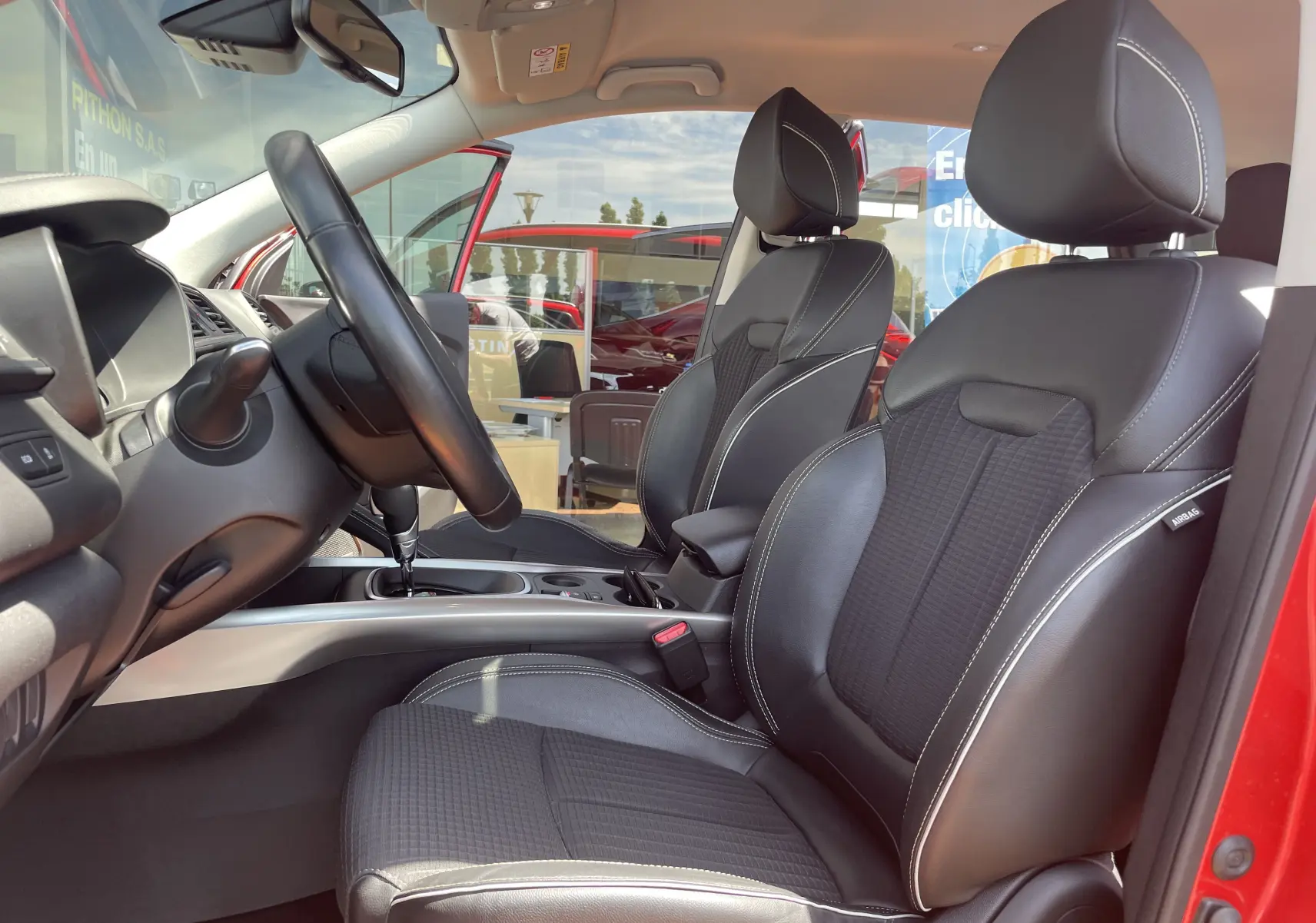 Vue intérieure côté conducteur du Renault Kadjar rouge flamme 2018, sièges en cuir noir avec surpiqûres blanches.