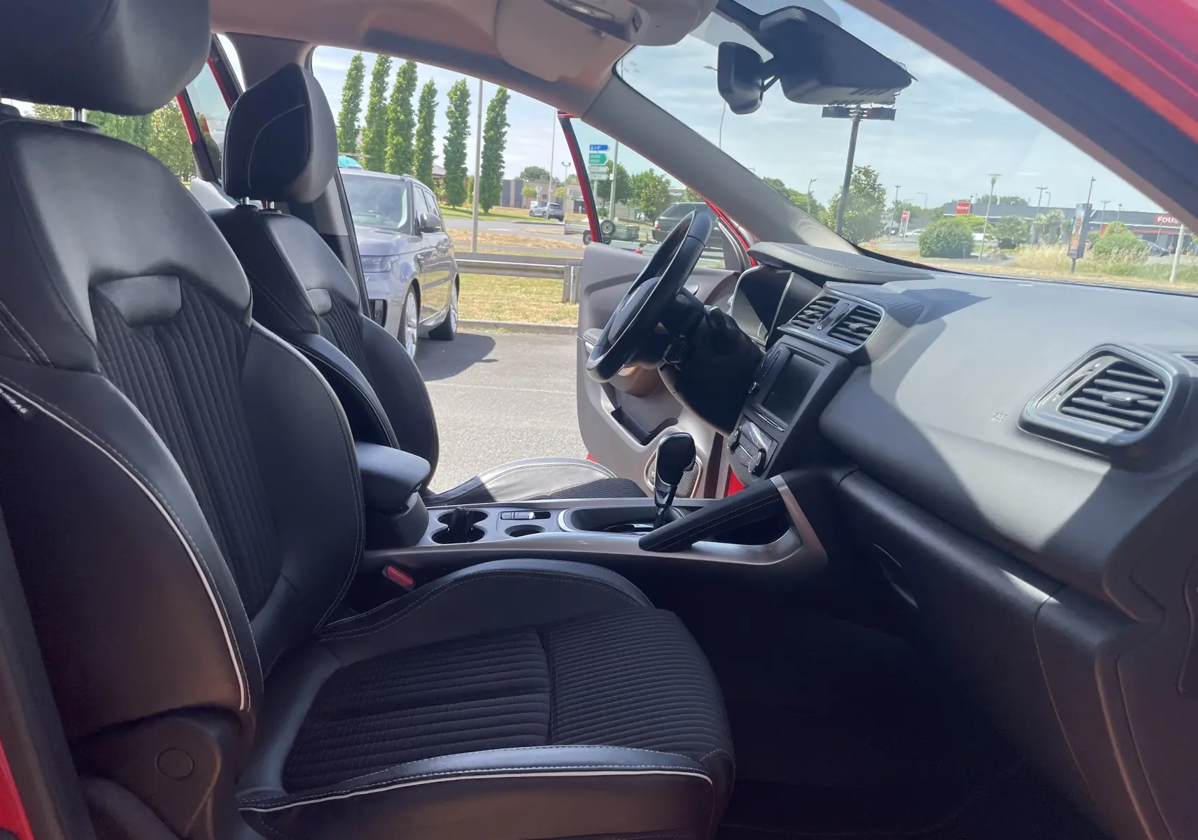 Vue intérieure côté conducteur du Renault Kadjar rouge flamme 2018, mettant en valeur les sièges noirs en cuir et la console centrale.