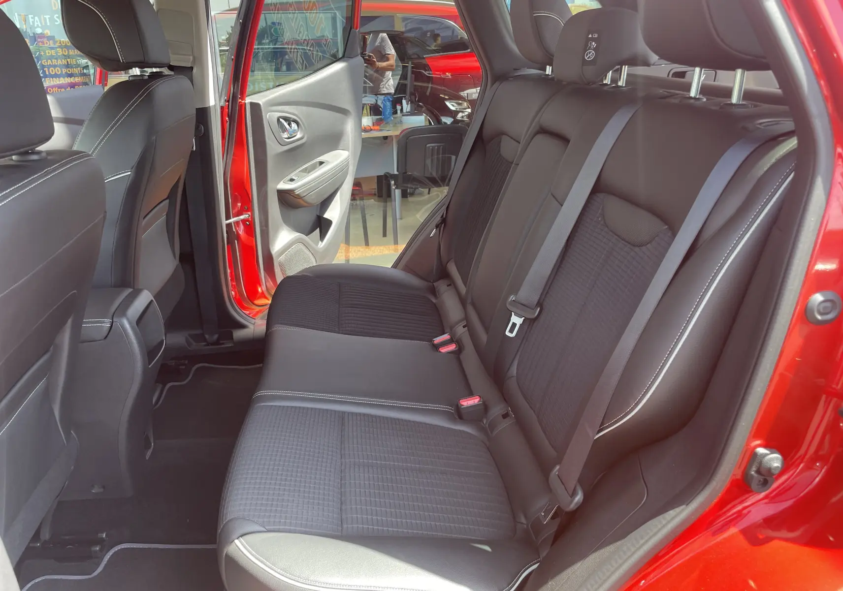 Vue intérieure arrière côté droit du Renault Kadjar rouge flamme, montrant les sièges arrière en tissu noir avec surpiqûres blanches.