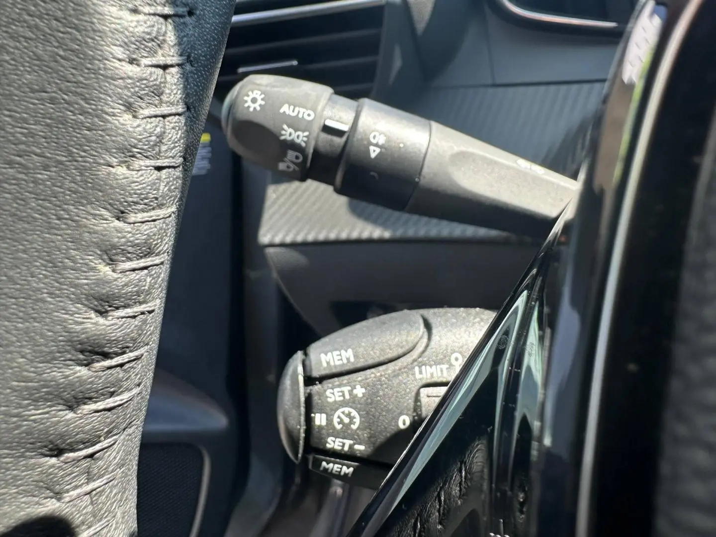 Détail des commandes au volant côté gauche sur Peugeot 208 1.2 100ch gris Selenium avec volant cuir noir.