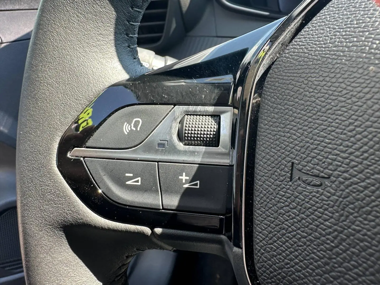 Gros plan sur les commandes du volant à gauche en plastique noir brillant de la Peugeot 208 2025, finition Gris Selenium.