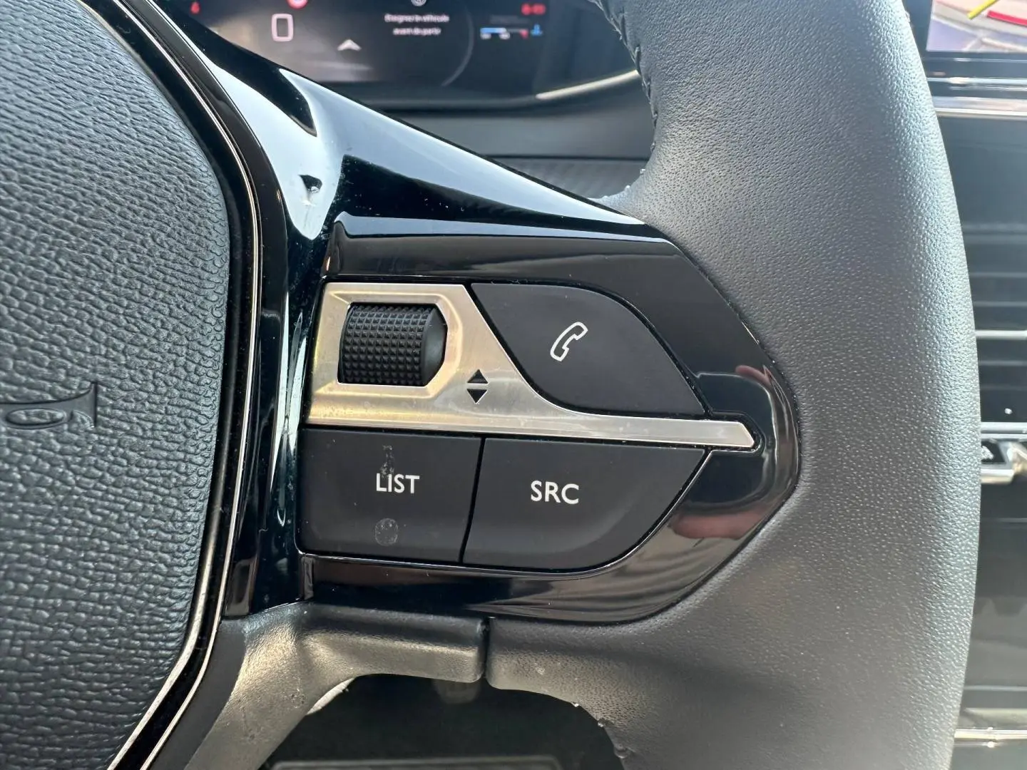 Gros plan sur les commandes gauche du volant noir de la Peugeot 208 2025, boutons appel et réglage audio visibles.