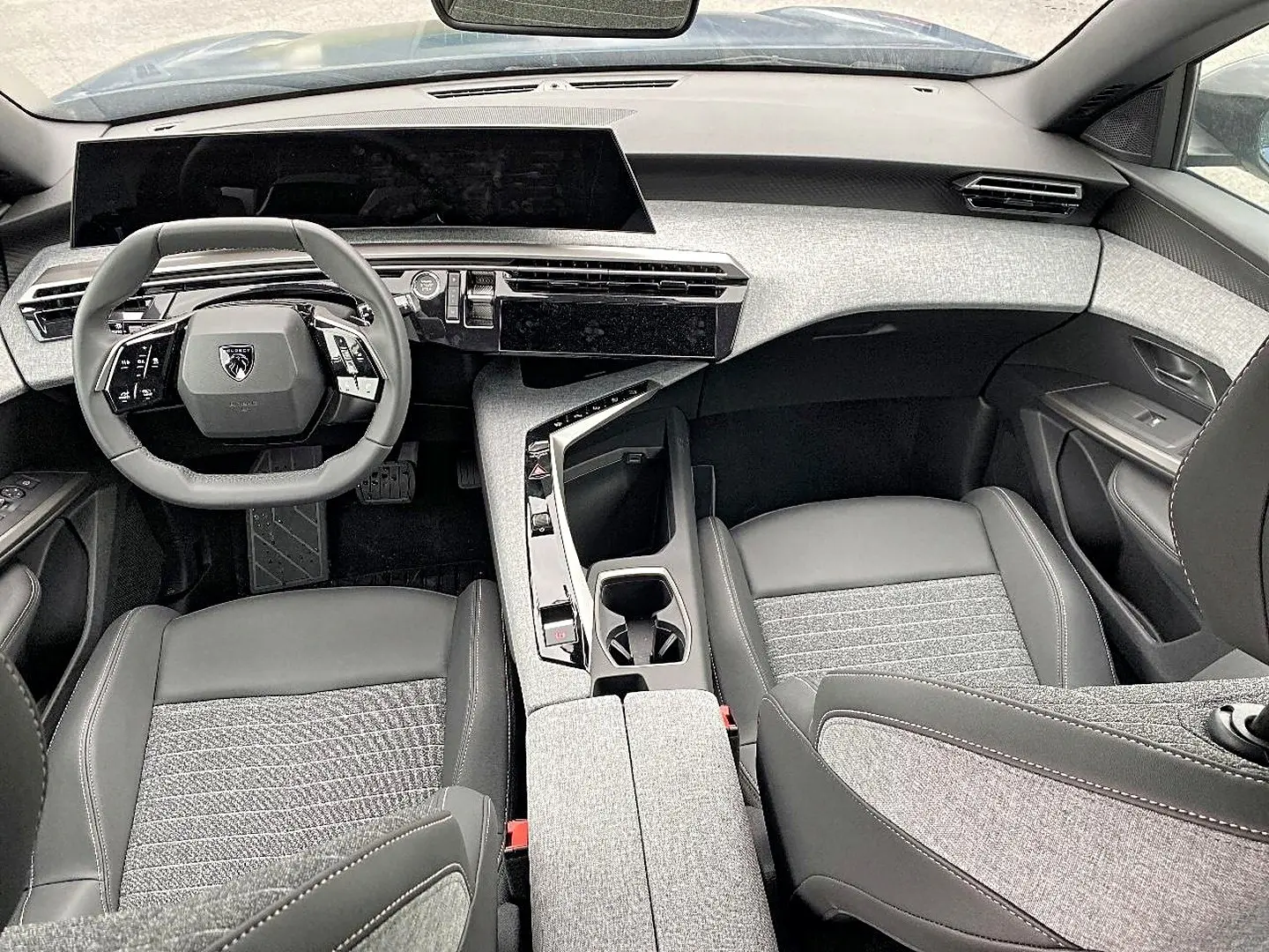 Vue intérieure avant du Peugeot 3008 bleu 2025, mettant en valeur le tableau de bord moderne et les sièges bi-matière gris et noir.