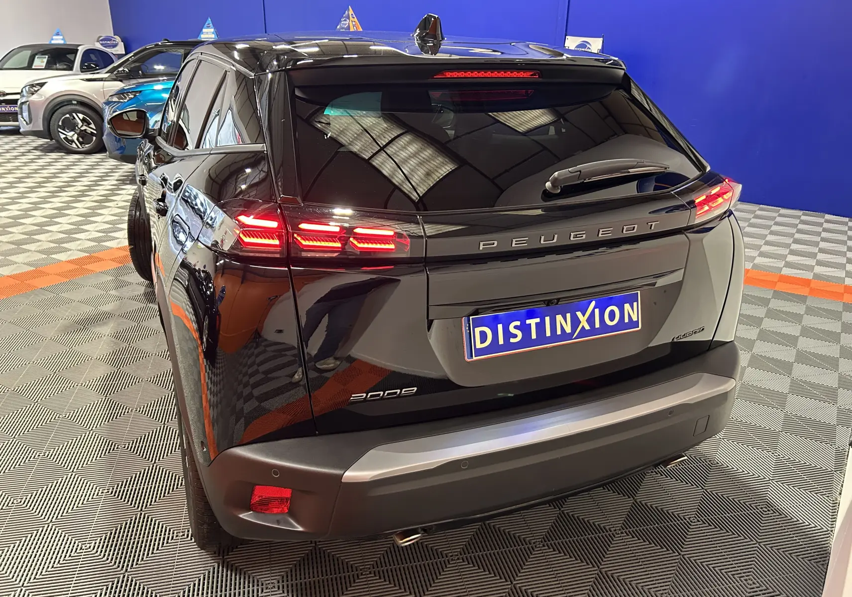 Vue 3/4 arrière d’un Peugeot 2008 noir avec feux arrière allumés dans un showroom au sol damier.