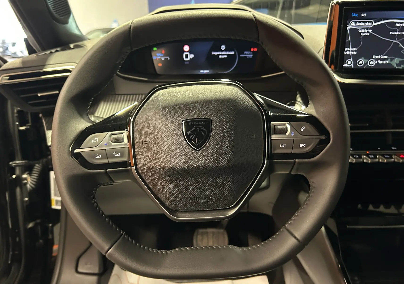 Vue rapprochée du volant noir de la Peugeot 2008 II Hybrid 110 avec tableau de bord digital et écran GPS visible.