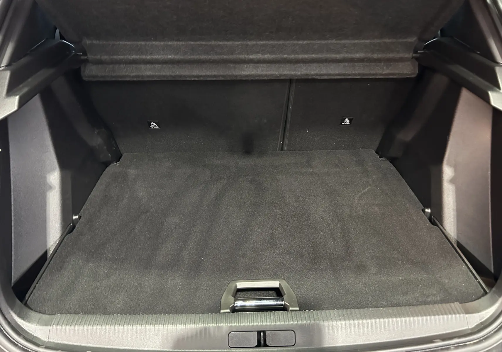Coffre spacieux et propre du Peugeot 2008 II Hybrid noir, vue intérieure depuis l'arrière avec plancher plat.