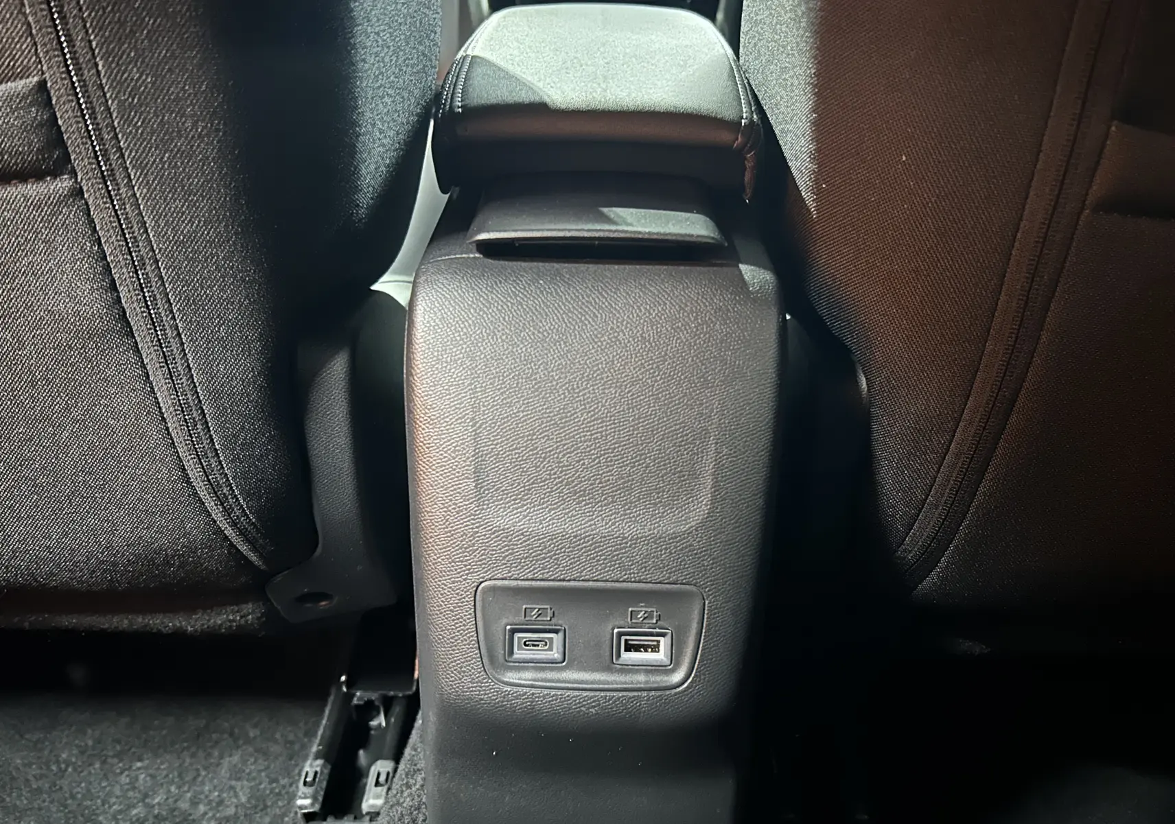 Vue rapprochée de la console centrale arrière noire du Peugeot 2008 II Hybrid avec ports USB-C et USB-A visibles.