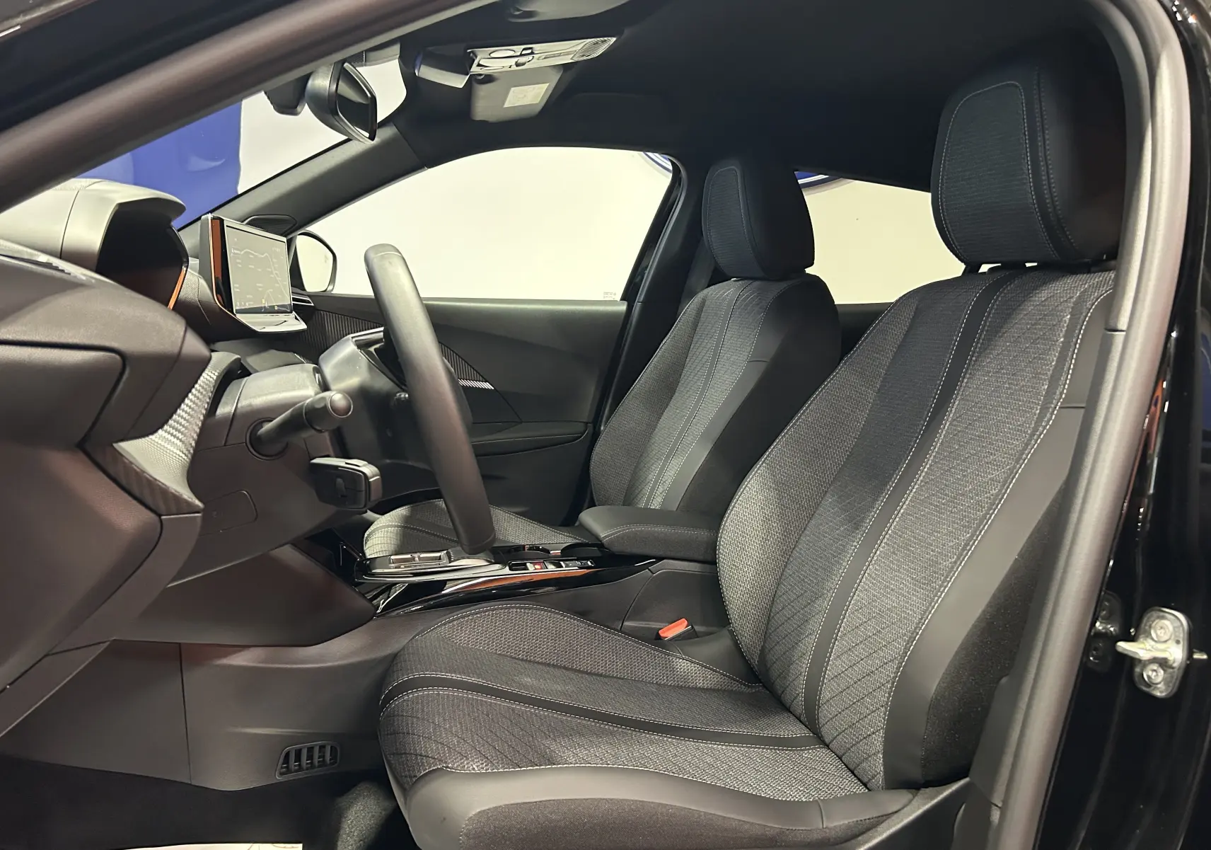 Vue intérieure côté conducteur du Peugeot 2008 noir, mettant en valeur les sièges avant et le tableau de bord moderne.