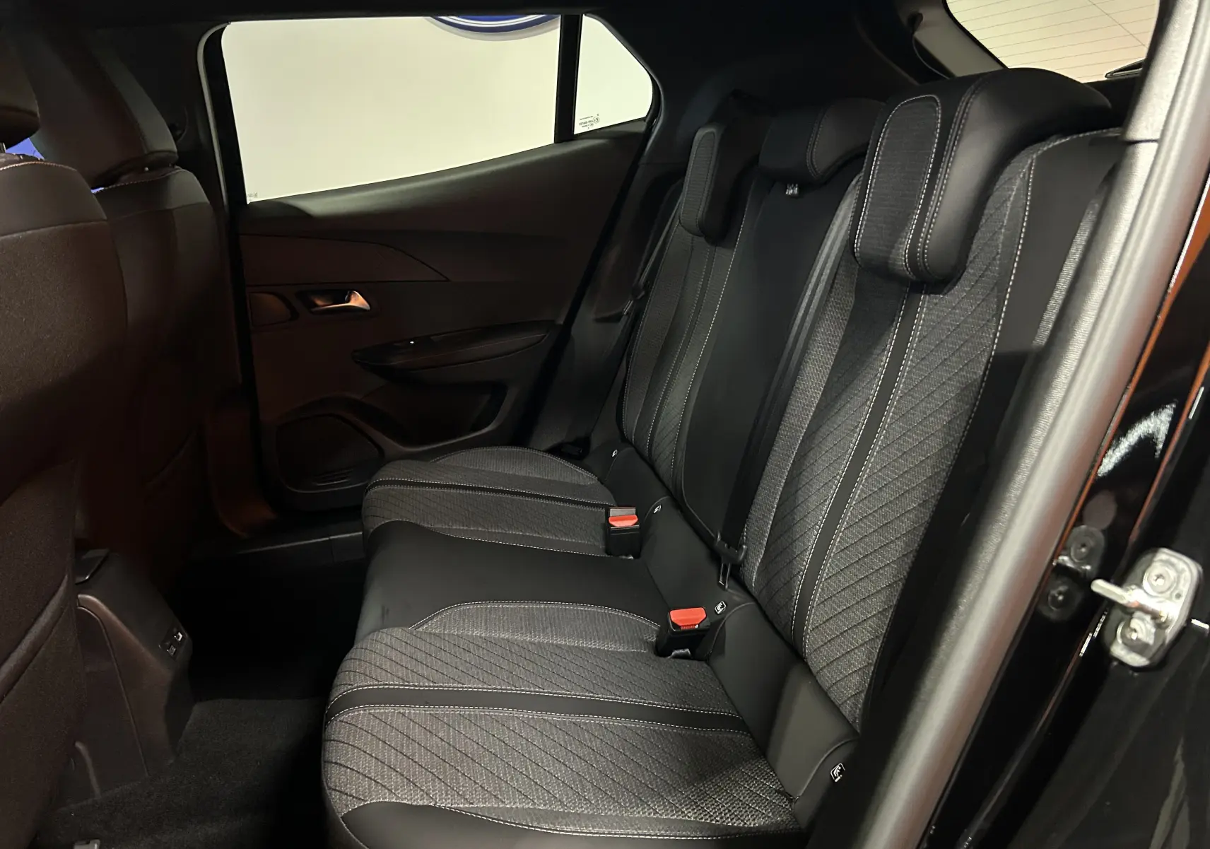 Vue intérieure côté droit des sièges arrière noirs du Peugeot 2008 II Hybrid 110 avec détails de couture contrastée.