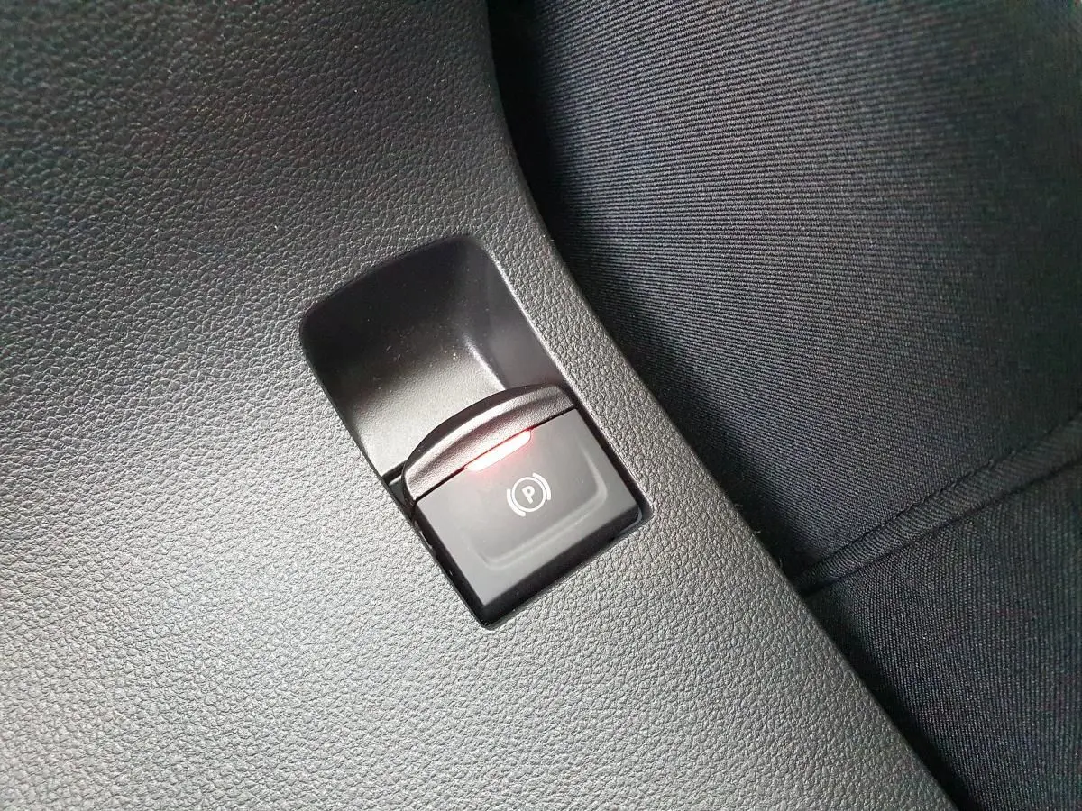 Gros plan sur le bouton de frein de parking électrique avec témoin rouge, intérieur noir du Dacia Jogger 2024.