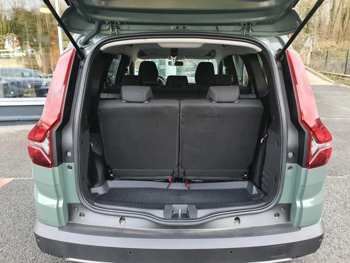 Vue arrière du Dacia Jogger 2024 en Licken Kaki, coffre ouvert montrant la banquette arrière noire et les feux arrière rouges.