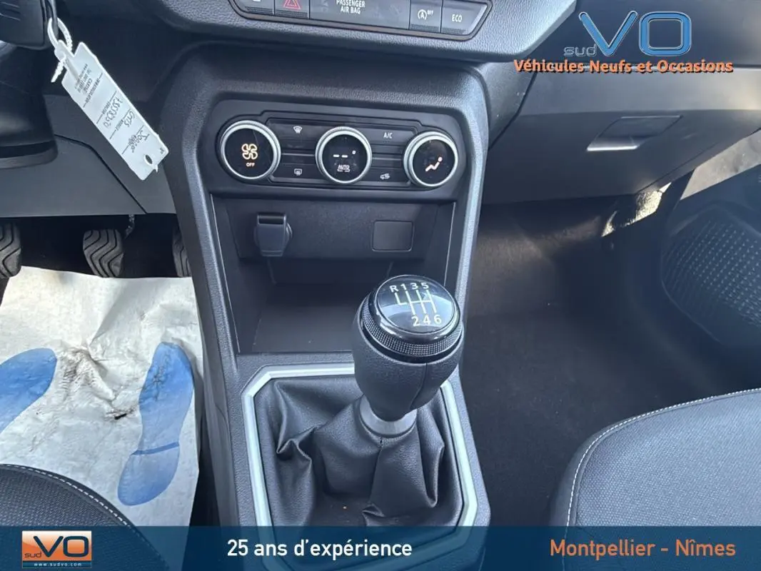 Gros plan sur le levier de vitesse manuel du Dacia Jogger gris, avec commandes de climatisation et console centrale visible.