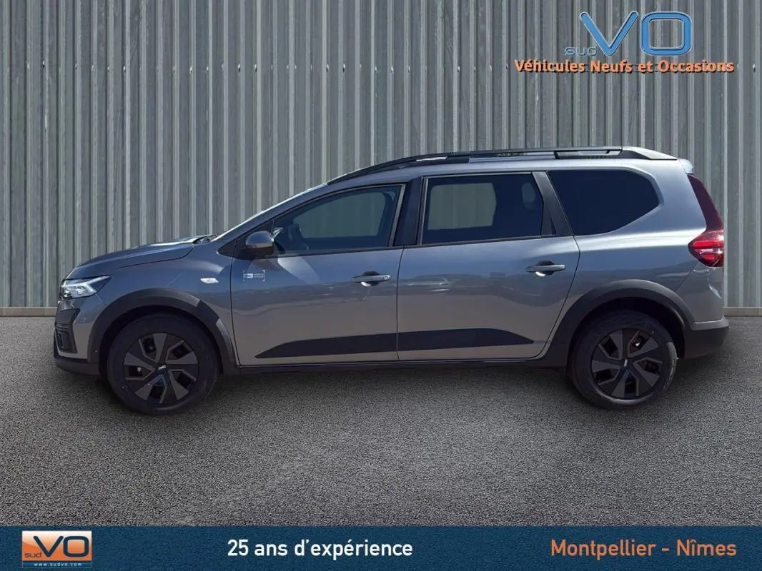 Vue de profil côté gauche d'un Dacia Jogger gris 2025 avec barres de toit et jantes noires.
