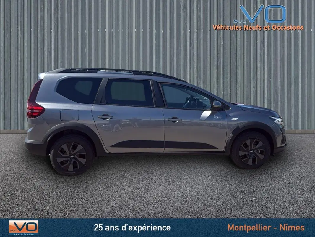 Profil côté droit du Dacia Jogger gris 2025 avec barres de toit et jantes noires, sur fond neutre extérieur.