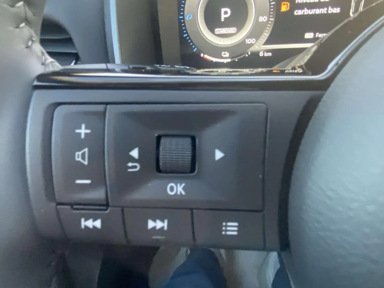 Gros plan sur les commandes au volant côté gauche du Nissan Qashqai gris Ceramic, tableau de bord numérique en arrière-plan.