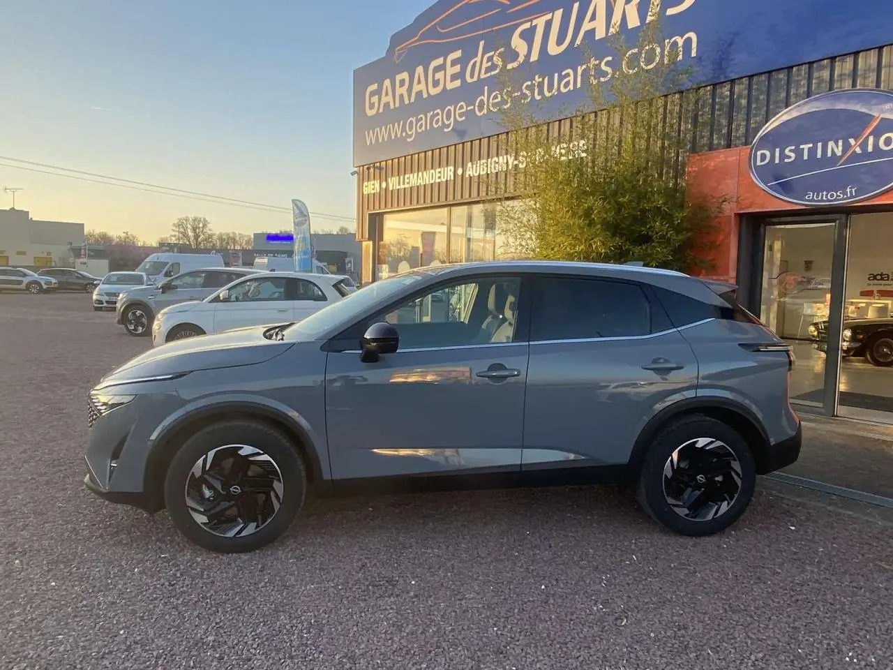 Vue de profil côté gauche d'un Nissan Qashqai gris ceramic garé devant un garage avec jantes noires au design moderne.
