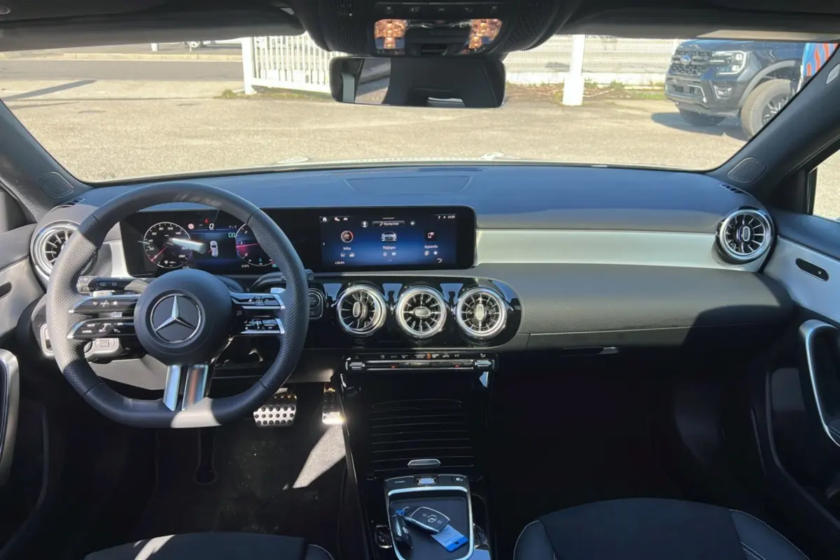 Vue intérieure frontale du tableau de bord de la Mercedes Classe A 200D Exclusive Design avec écran large et volant cuir multifonctions.