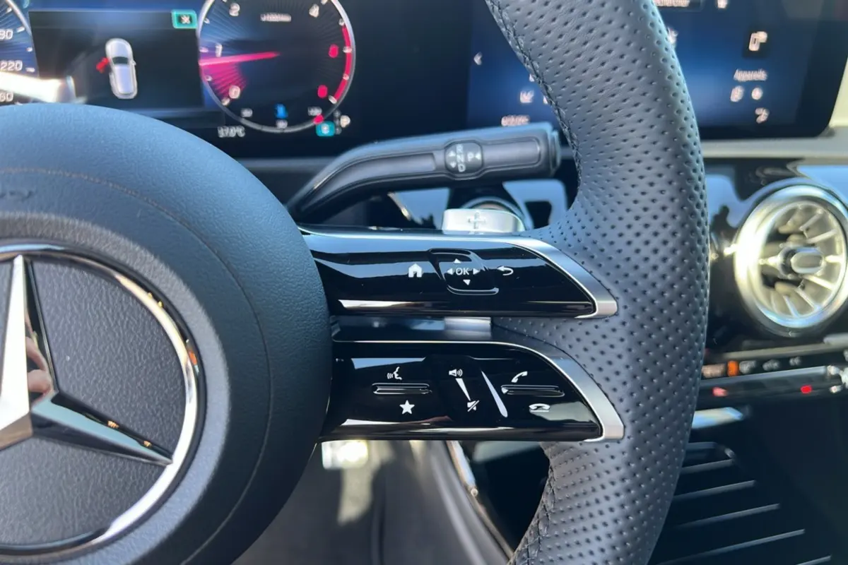 Gros plan sur le volant cuir perforé à commandes multifonctions d’une Mercedes Classe A 200D 2026, tableau de bord digital en arrière-plan.