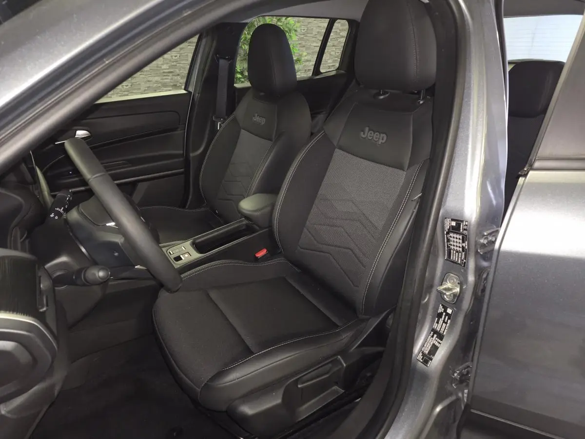 Vue intérieure côté conducteur du Jeep Avenger gris 2025, sièges noirs avec logo Jeep brodé sur appuie-tête.