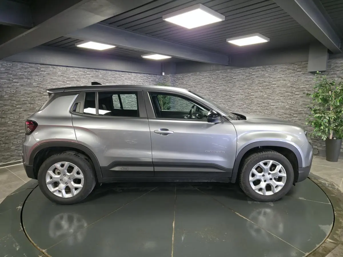 Vue de profil côté gauche d'un Jeep Avenger gris métallisé avec jantes alliage 17 pouces dans un showroom.