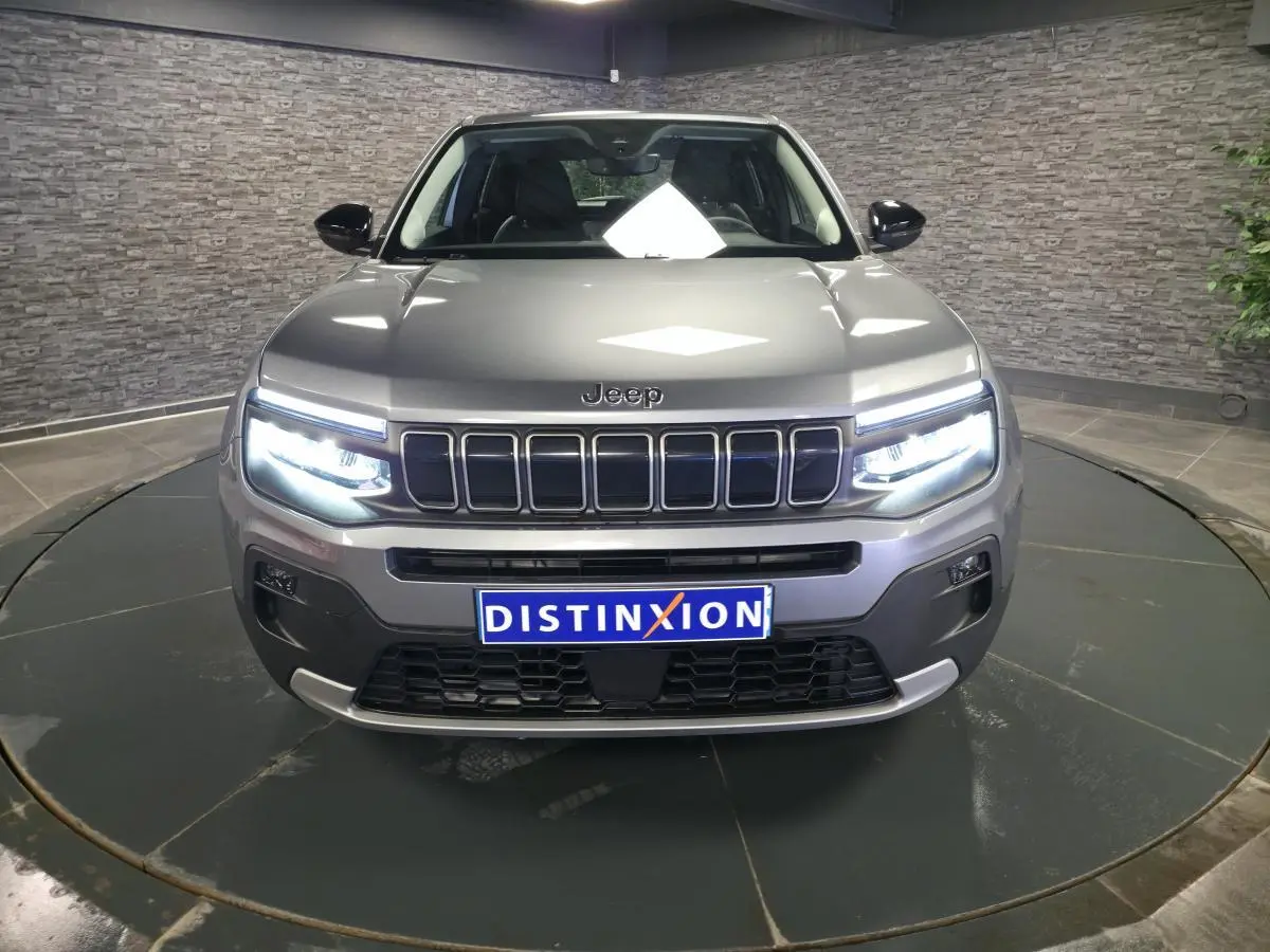 Vue frontale du Jeep Avenger gris avec phares LED allumés et calandre distinctive à sept fentes.