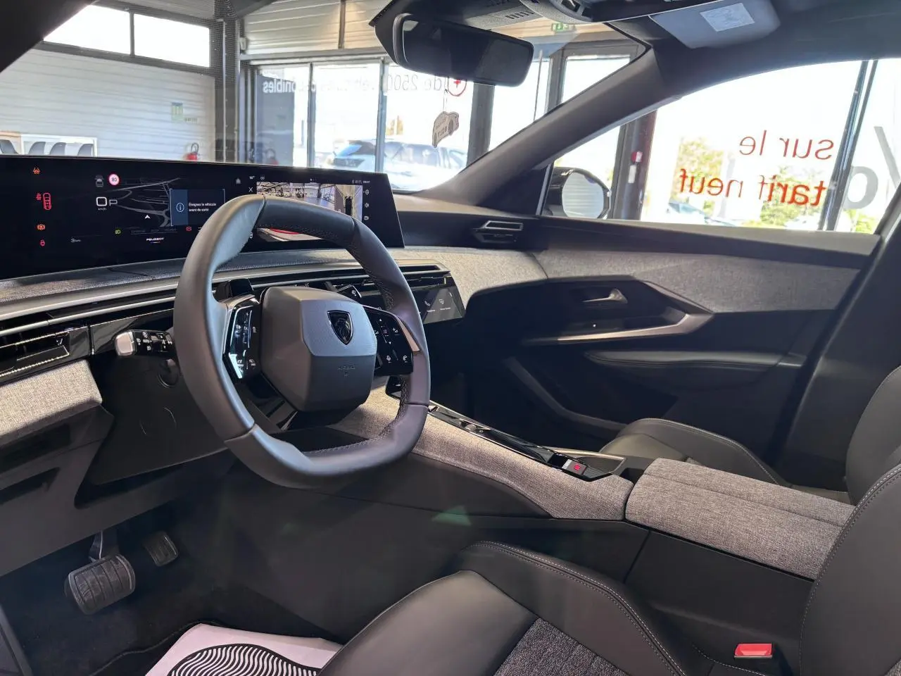 Vue intérieure côté conducteur du Peugeot 3008 hybride 2026, avec volant compact, tableau de bord numérique et habillage tissu gris.