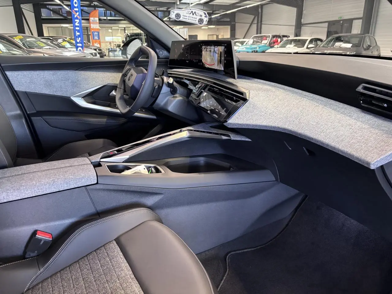 Vue intérieure côté conducteur du Peugeot 3008 Hybrid 2026, tableau de bord avec écran incurvé et décor tissu gris chiné.