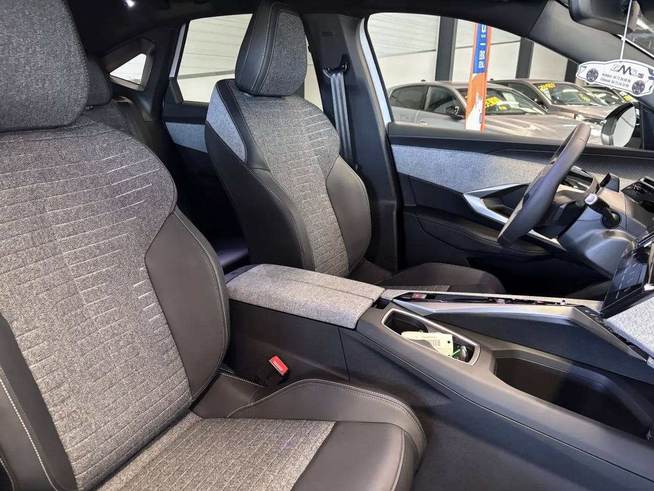 Vue intérieure côté droit du Peugeot 3008 Hybrid 2026, sièges tissu gris et cuir noir avec console centrale assortie.