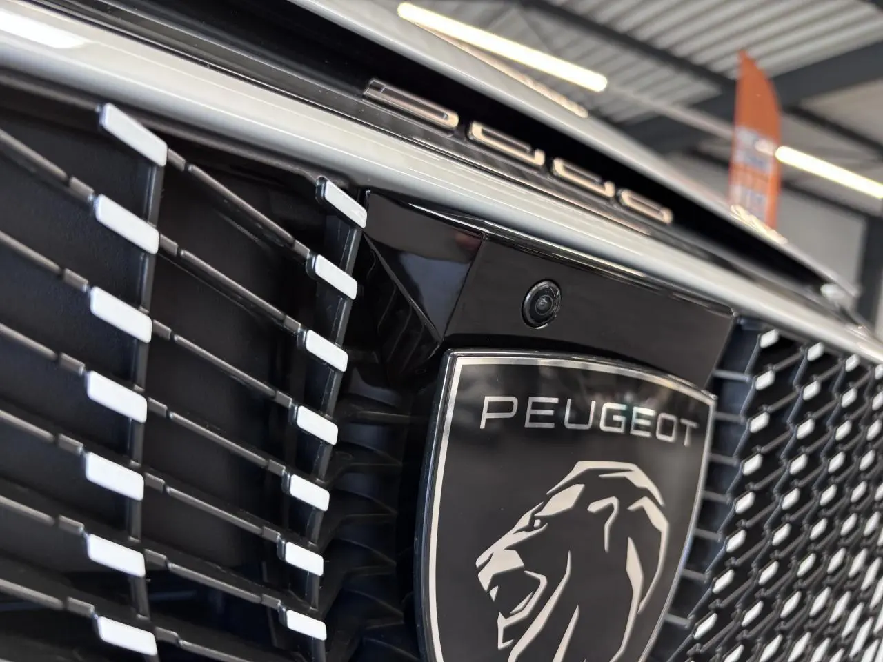 Gros plan sur la calandre noire laquée du Peugeot 3008 blanc avec logo lion et inscription Peugeot en chrome.