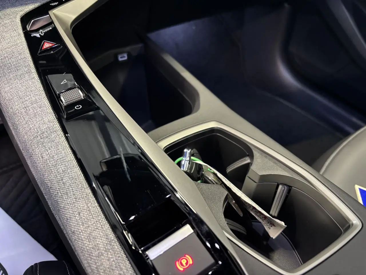 Gros plan sur la console centrale noire laquée et tissu gris chiné du Peugeot 3008 hybride avec frein de stationnement électrique activé.