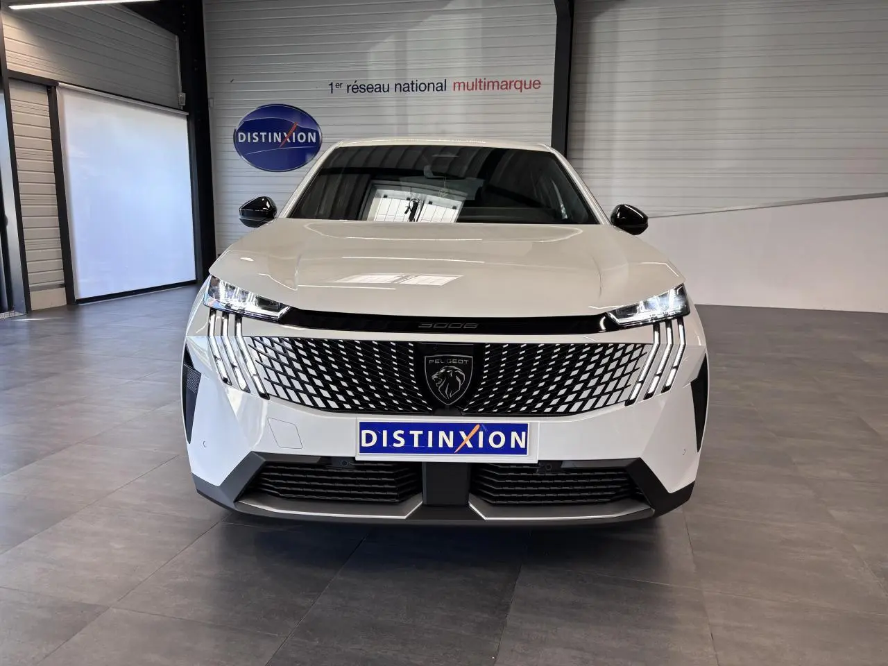 Vue avant d’un Peugeot 3008 blanc avec calandre noire laquée et feux LED 3 griffes, en intérieur showroom.
