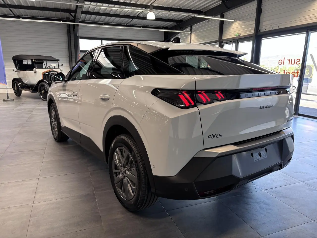 Vue 3/4 arrière droite du Peugeot 3008 blanc hybride avec feux arrière LED à 3 griffes et bandeau noir laqué.