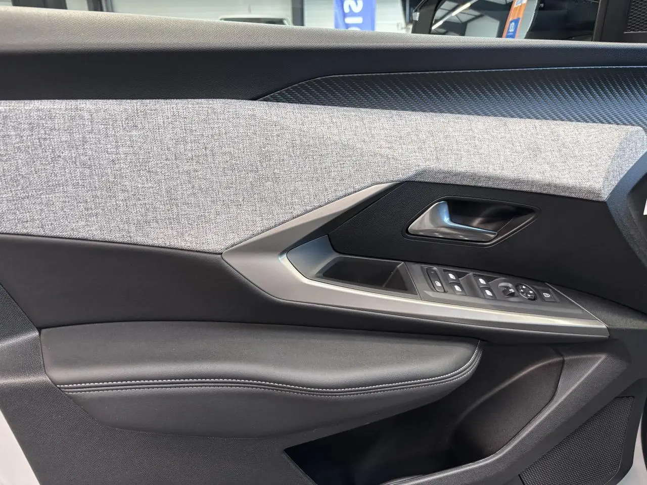 Gros plan sur la garniture intérieure de porte côté gauche du Peugeot 3008 blanc, avec tissu gris et commandes électriques.