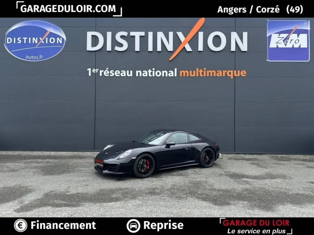 Vue 3/4 avant droite d'une Porsche 911 Carrera GTS Coupé noire avec jantes noires et étriers rouges, stationnée devant un mur gris.