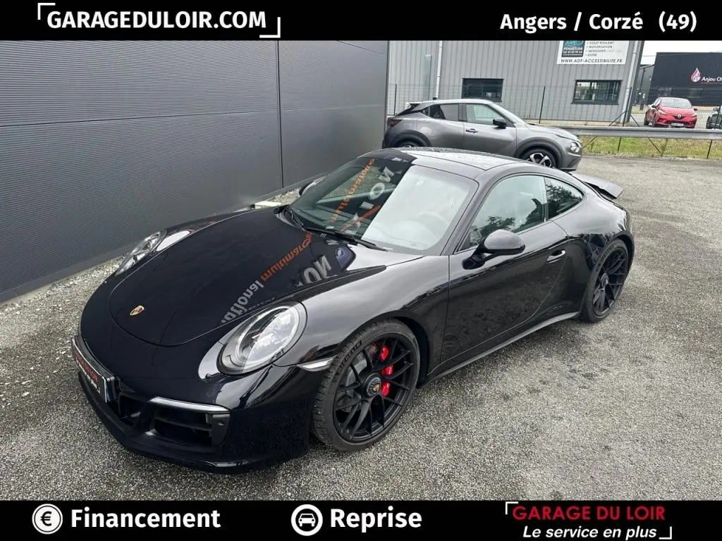 Vue 3/4 avant droite d'une Porsche 911 Carrera GTS Coupé noire avec jantes noires et étriers rouges, stationnée sur sol gravillonné.