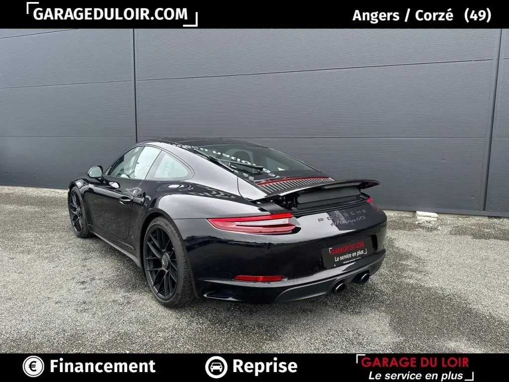 Vue 3/4 arrière droite d'une Porsche 911 Carrera GTS Coupé noire avec aileron arrière déployé sur sol gris.