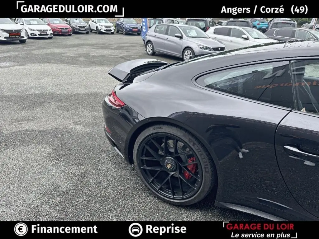 Vue 3/4 arrière droite d'une Porsche 911 Carrera GTS Coupé noire avec aileron arrière relevé et jantes noires.