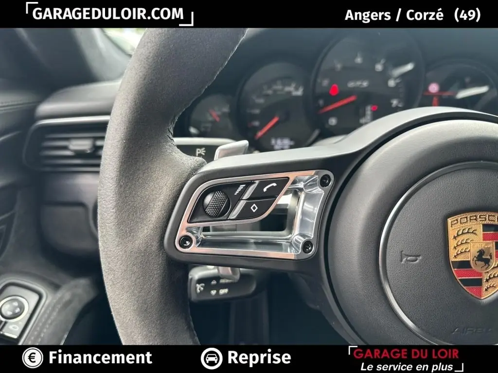 Gros plan sur le volant en alcantara côté gauche avec commandes intégrées et logo Porsche visible au centre.