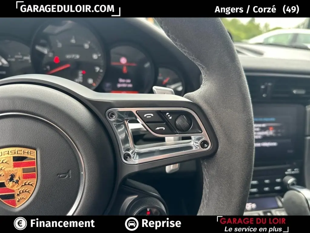 Gros plan sur le volant en alcantara côté droit avec commandes et logo Porsche visible, intérieur noir de la 911 Carrera GTS.
