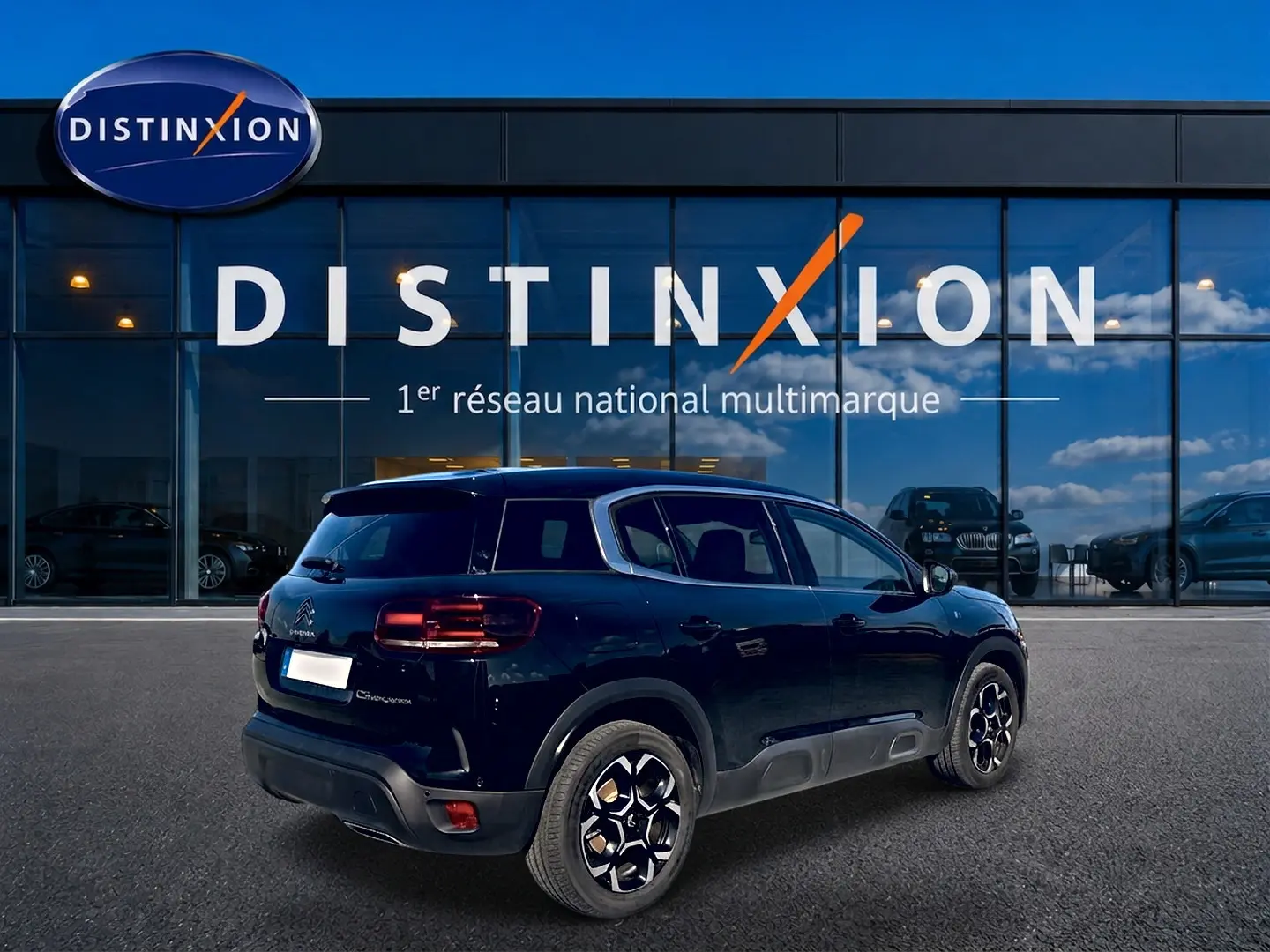 Vue 3/4 arrière droite d'un Citroën C5 Aircross noir 2024 avec jantes alu et barres de toit devant un showroom Distinxion.
