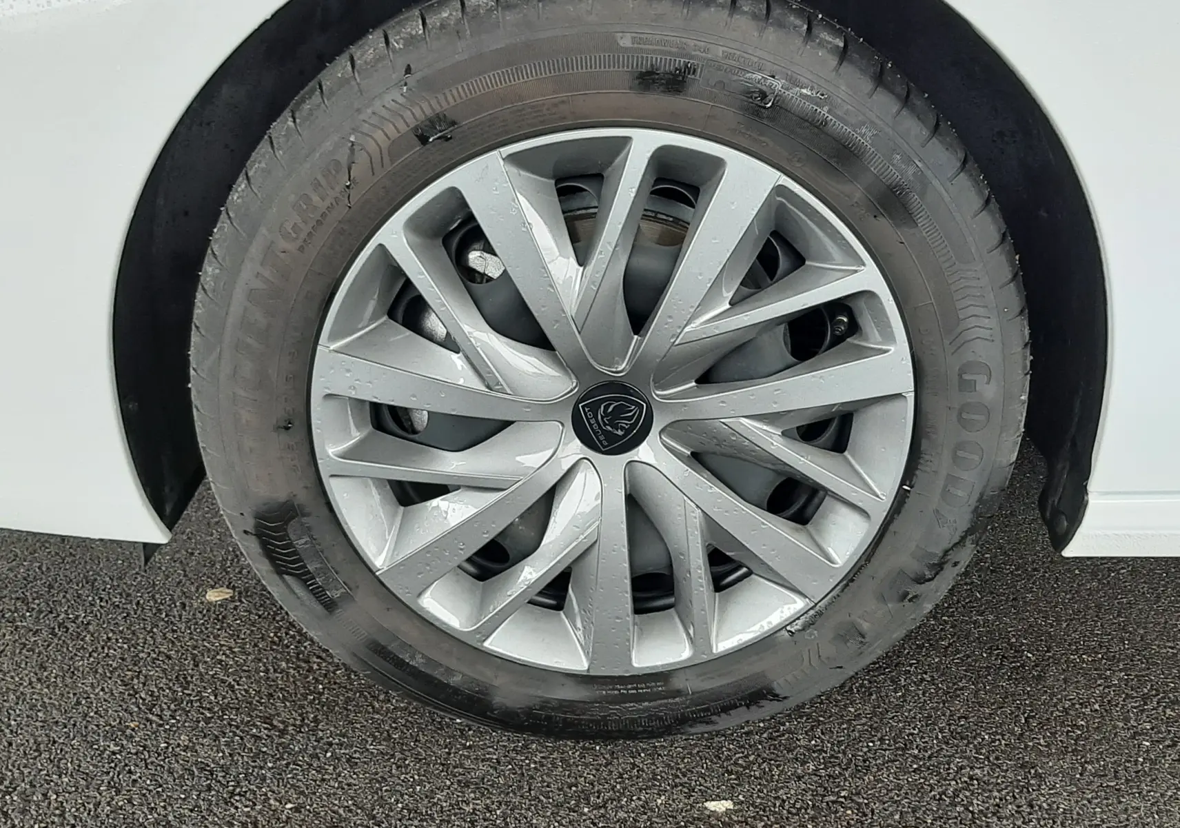 Gros plan sur la roue avant droite d'une Peugeot 308 blanche avec jante alliage argentée et logo Peugeot central.