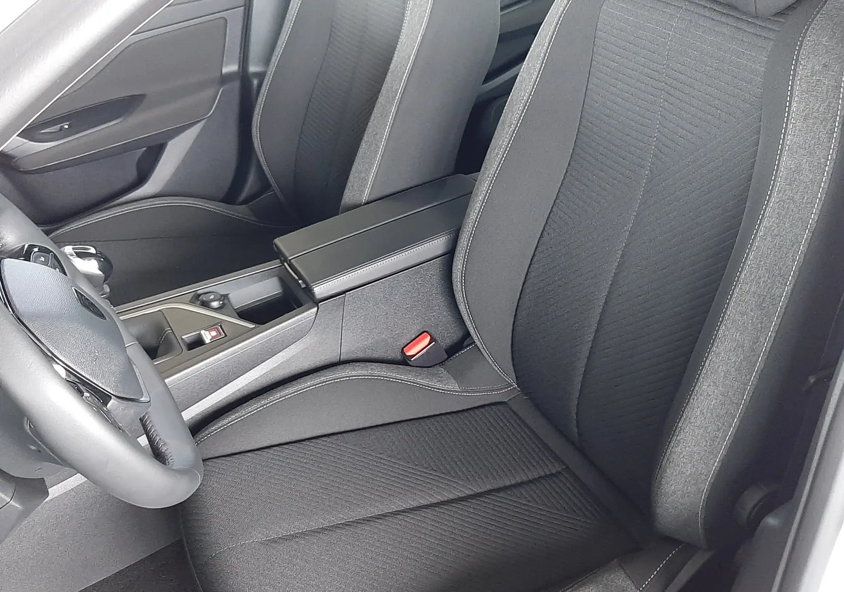 Vue intérieure côté conducteur de la Peugeot 308 2022 avec sièges tissu noir et accoudoir central.