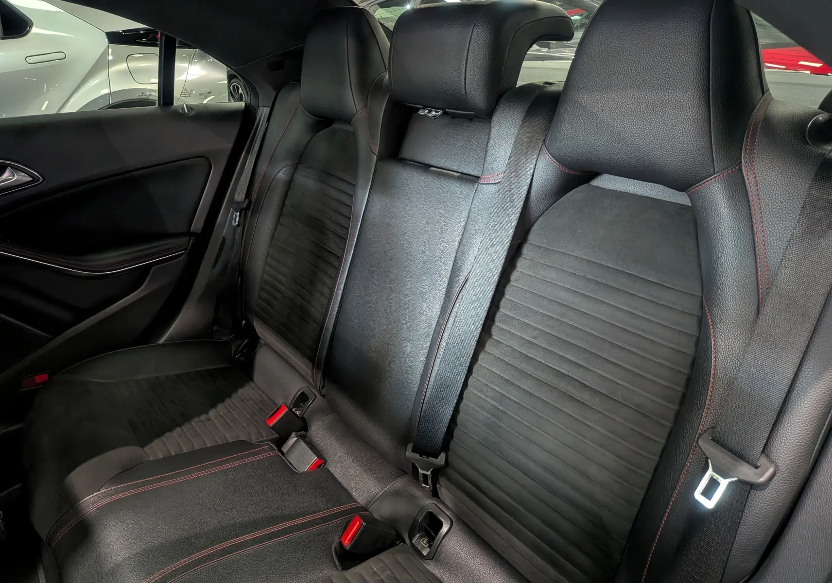 Vue intérieure des sièges arrière en cuir noir avec surpiqûres rouges d'une Mercedes CLA 200 Fascination 2017.