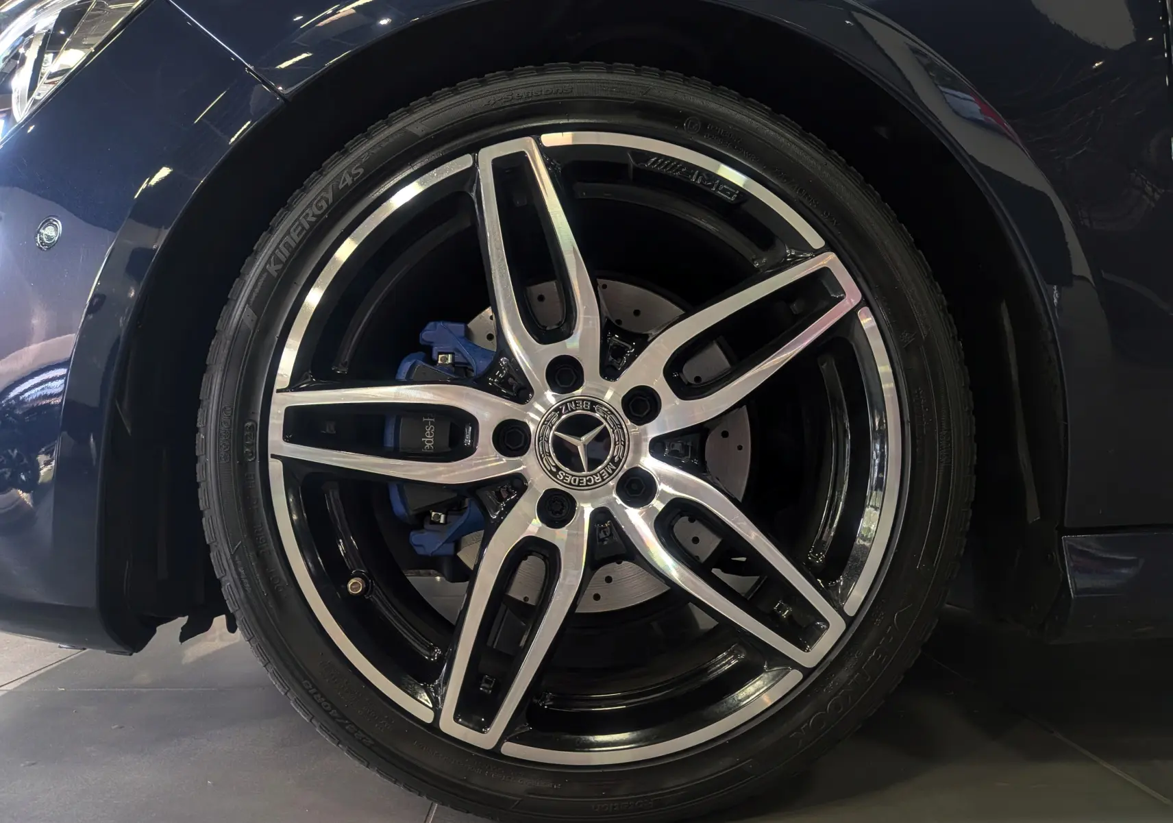 Gros plan sur la roue avant gauche d'une Mercedes Classe CLA 200 Fascination bleu Cavansite avec jante AMG 18 pouces bicolore.