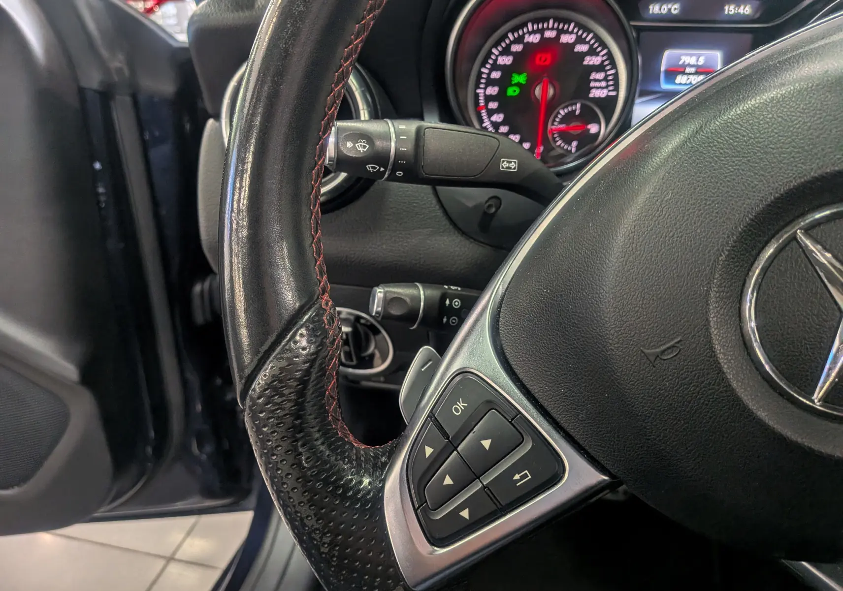 Vue rapprochée du volant cuir noir avec commandes intégrées et tableau de bord éclairé d'une Mercedes Classe CLA 2017.