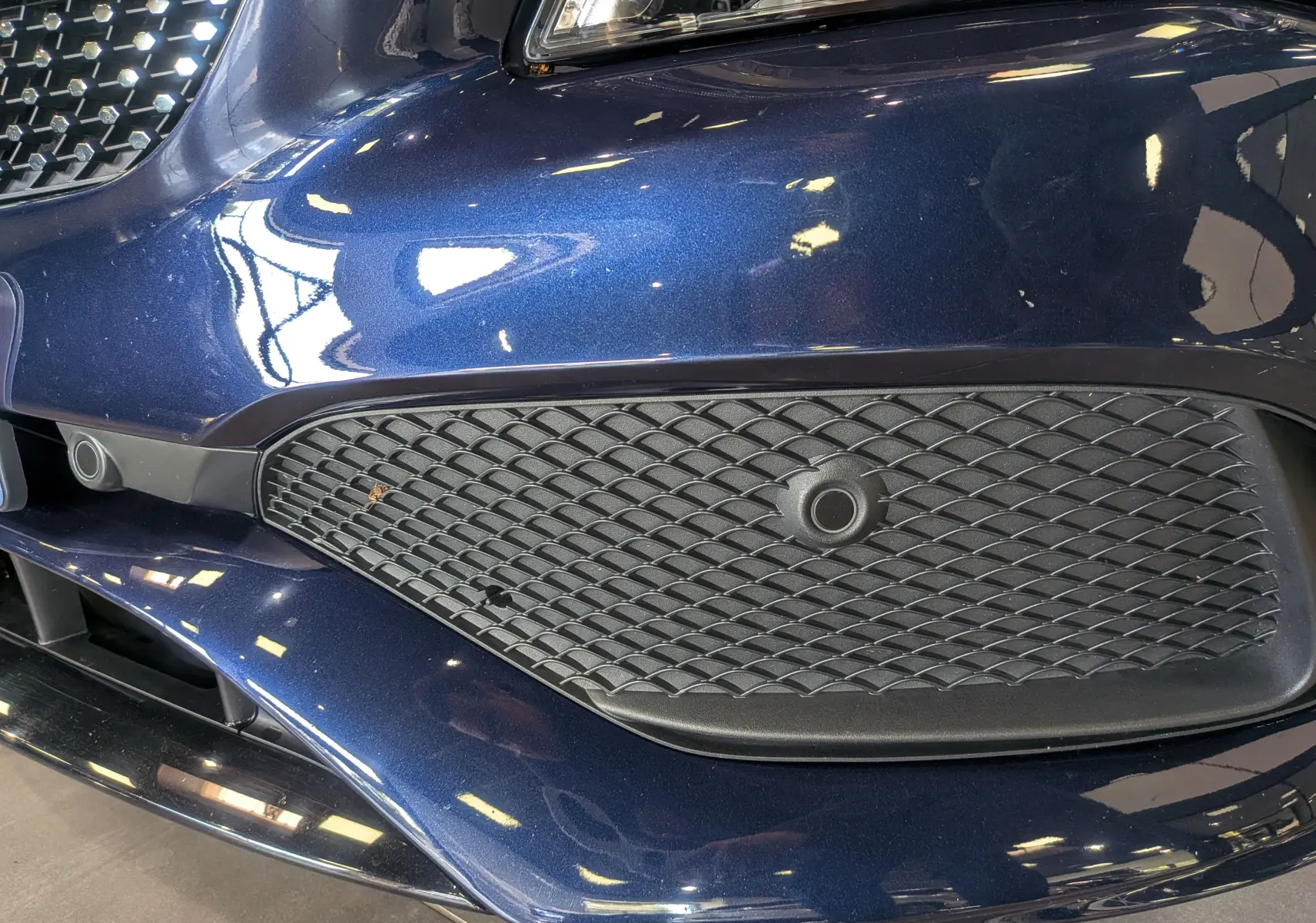 Gros plan sur la calandre avant droite bleu Cavansite d'une Mercedes CLA 200 Fascination 2017 avec capteur de stationnement intégré.