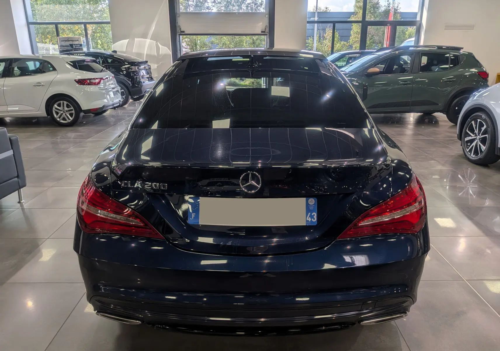Vue arrière d'une Mercedes Classe CLA 200 bleu Cavansite dans un showroom, avec feux arrière rouges et logo Mercedes visible.