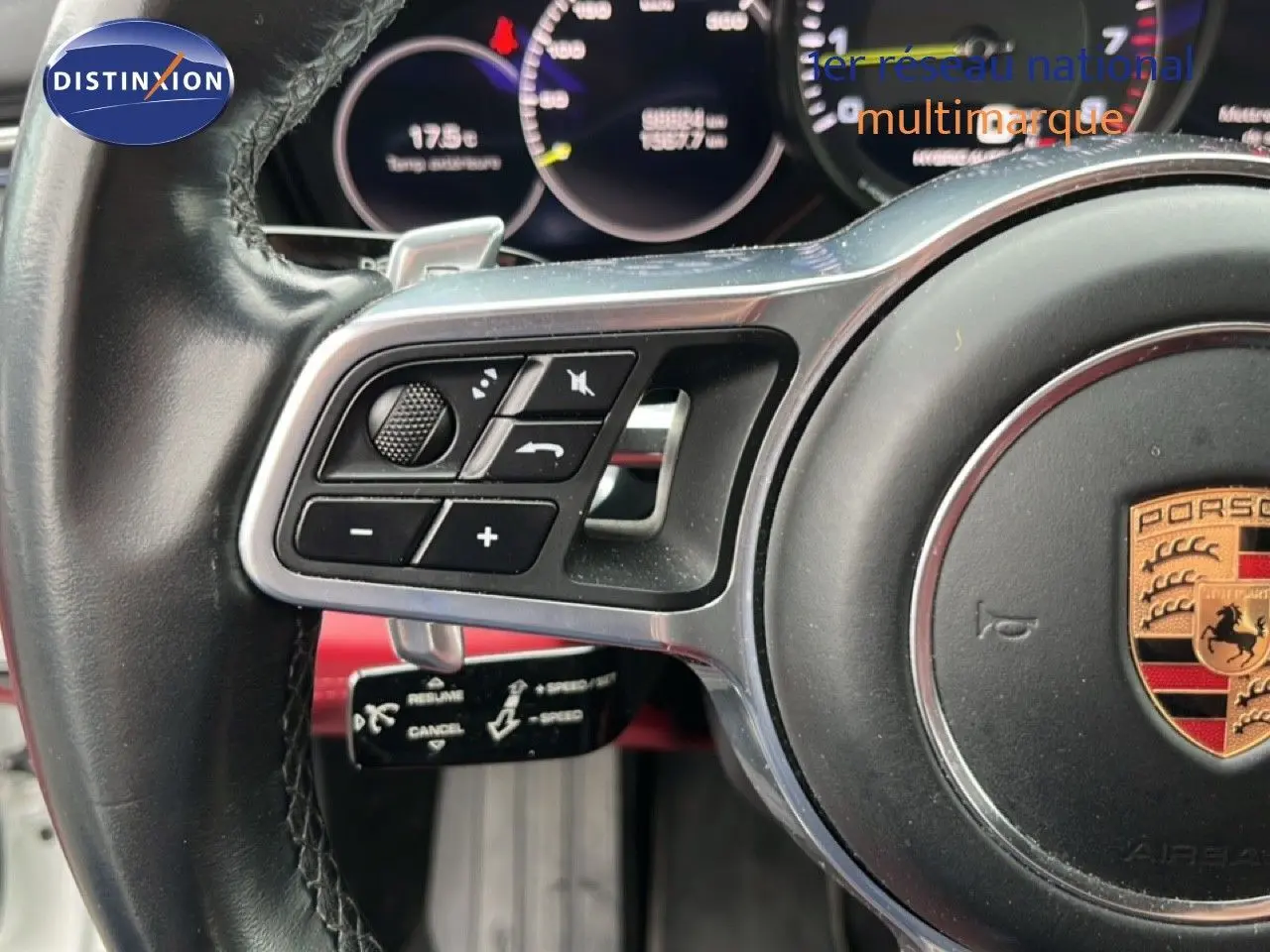 Gros plan sur le volant noir multifonction avec logo Porsche, montrant les commandes et palettes de la Panamera 4 E-Hybrid blanche.