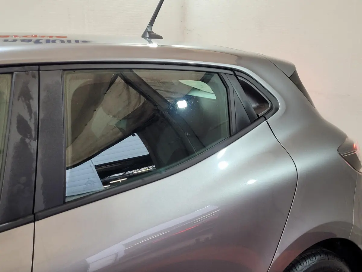 Vue latérale côté gauche sur l'arrière d'une Renault Clio gris foncé 2025 avec vitre teintée et antenne toit.