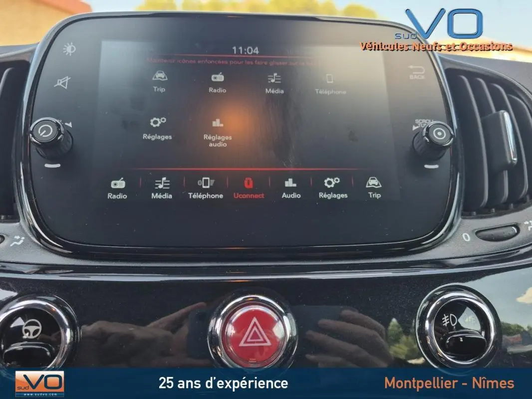 Vue rapprochée de l'écran tactile et des commandes centrales du tableau de bord d'une Fiat 500C noire 2024.